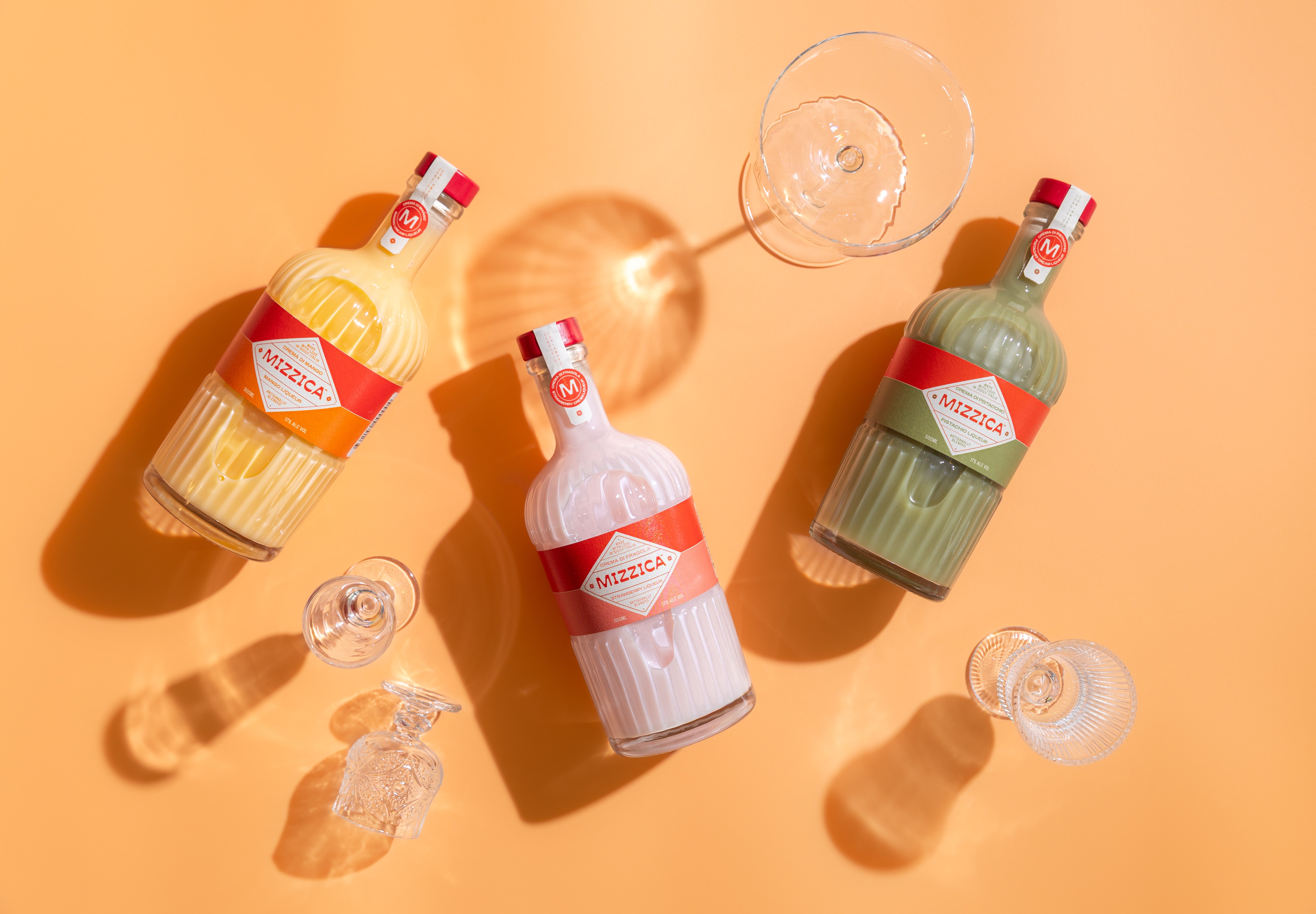 Three bottles of Mizzica liqueurs on a yellow background with glasses.