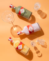 Three bottles of mizzica liqueur on a yellow background with glasses.