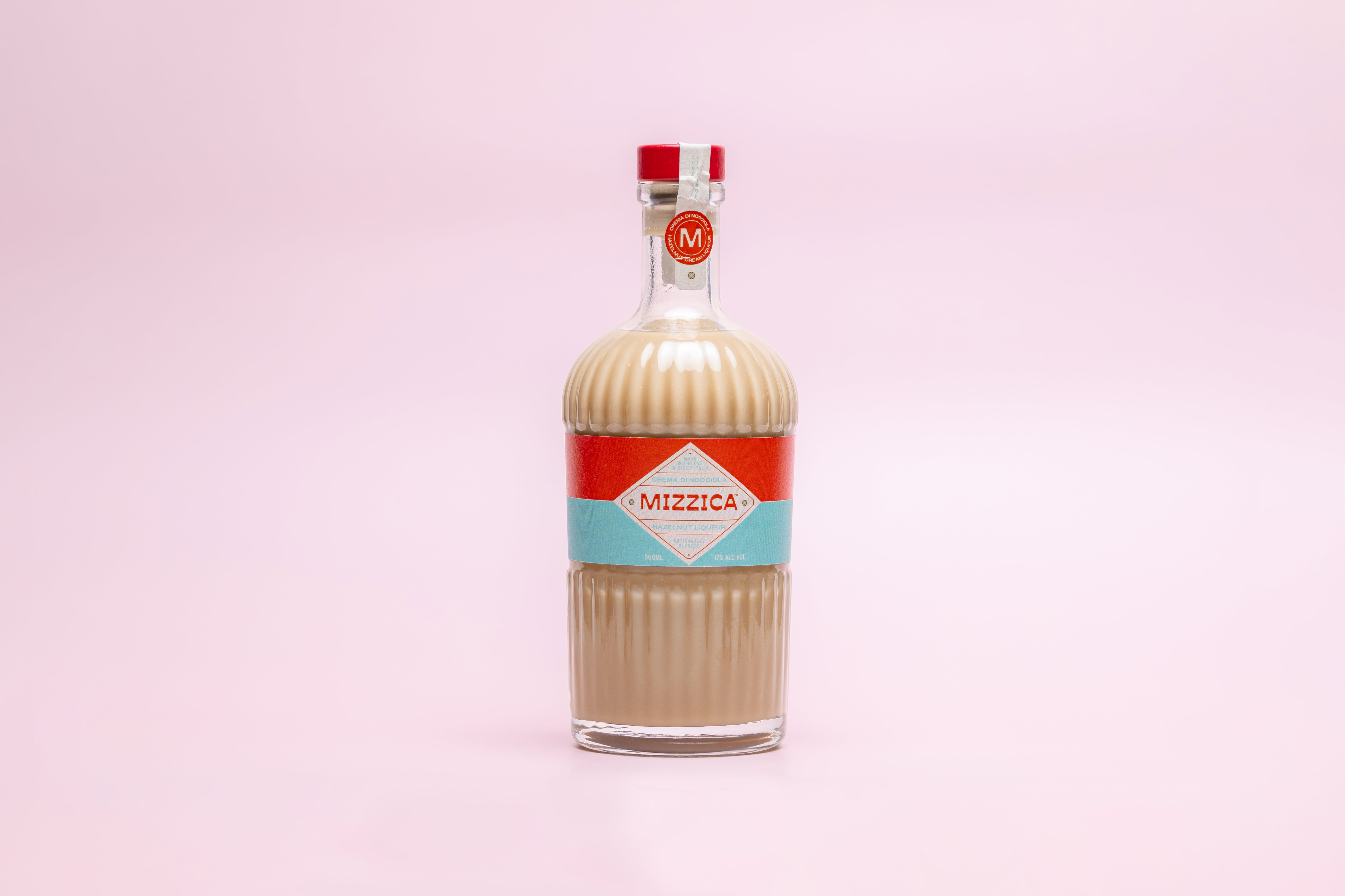 Bottle of Mizzica hazelnut liqueur on a pink background