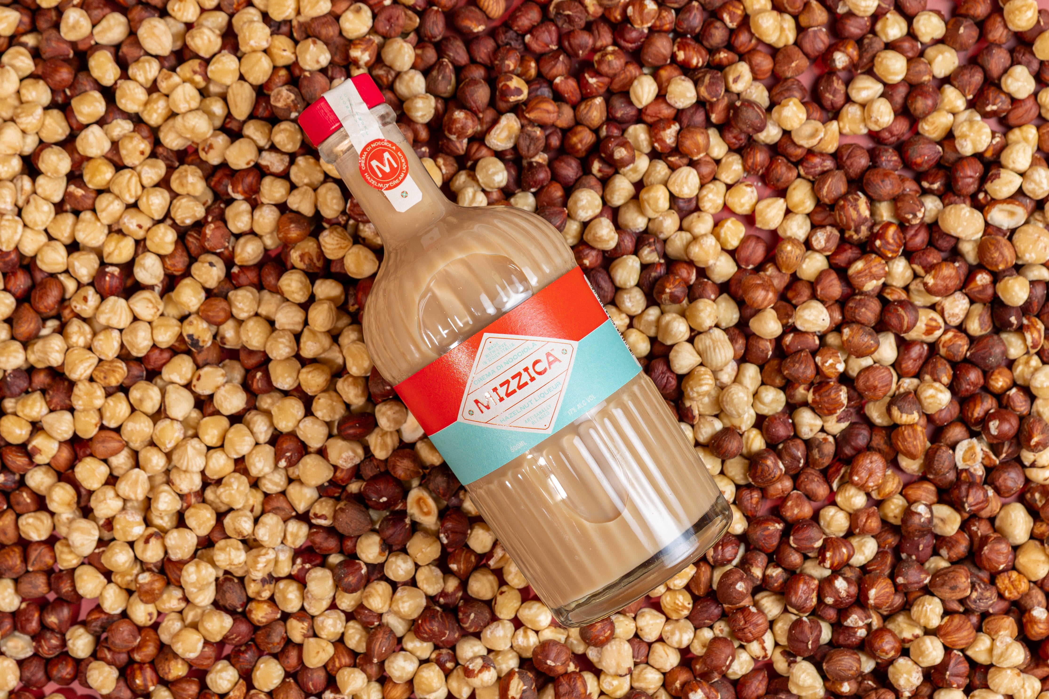 Bottle of Mizzica hazelnut liqueur on a bed of hazelnuts