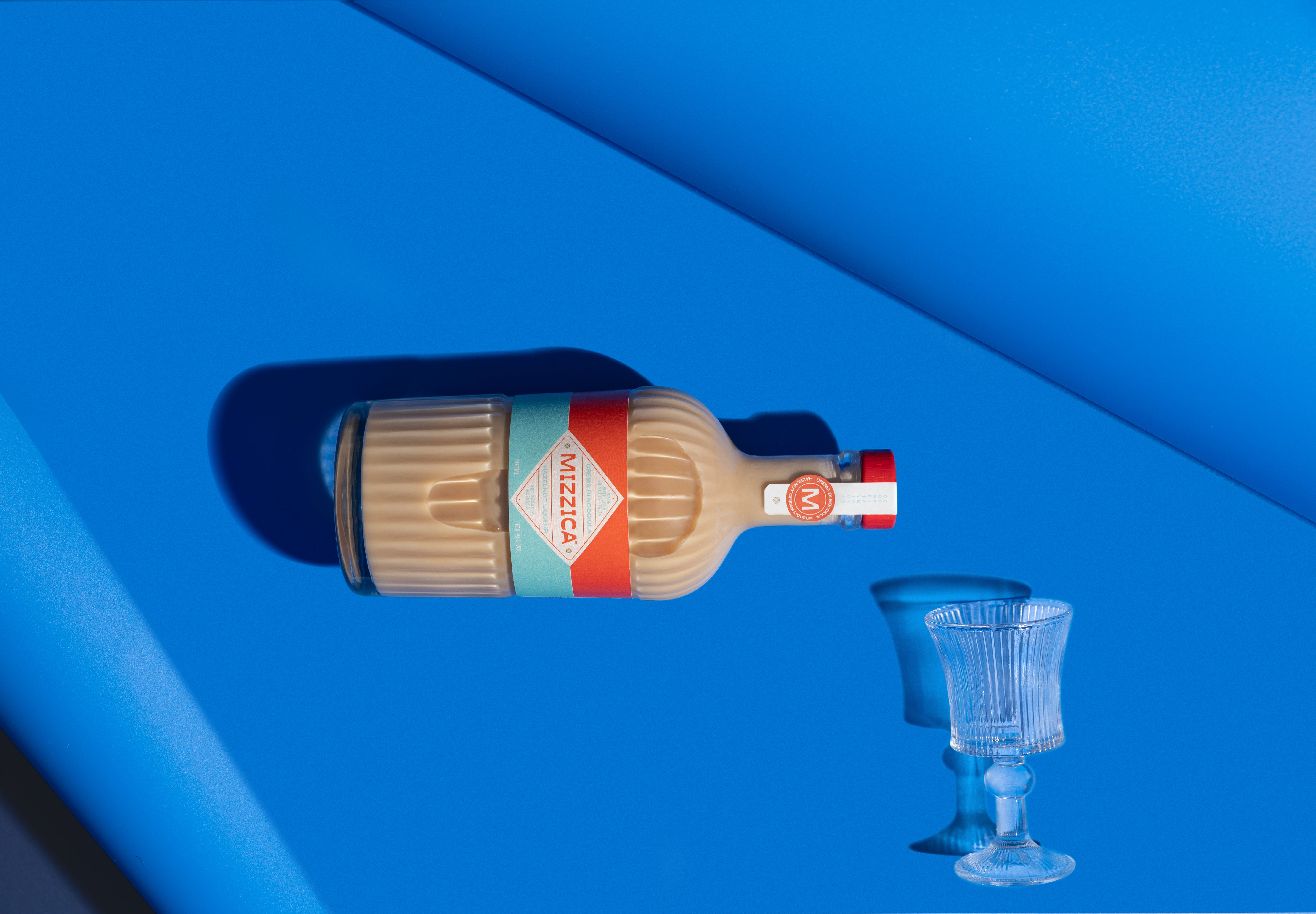 Bottle of Mizzica hazelnut liqueur with a glass on a blue background