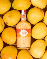 Mizzica bottle surrounded by mangoes on a wooden surface