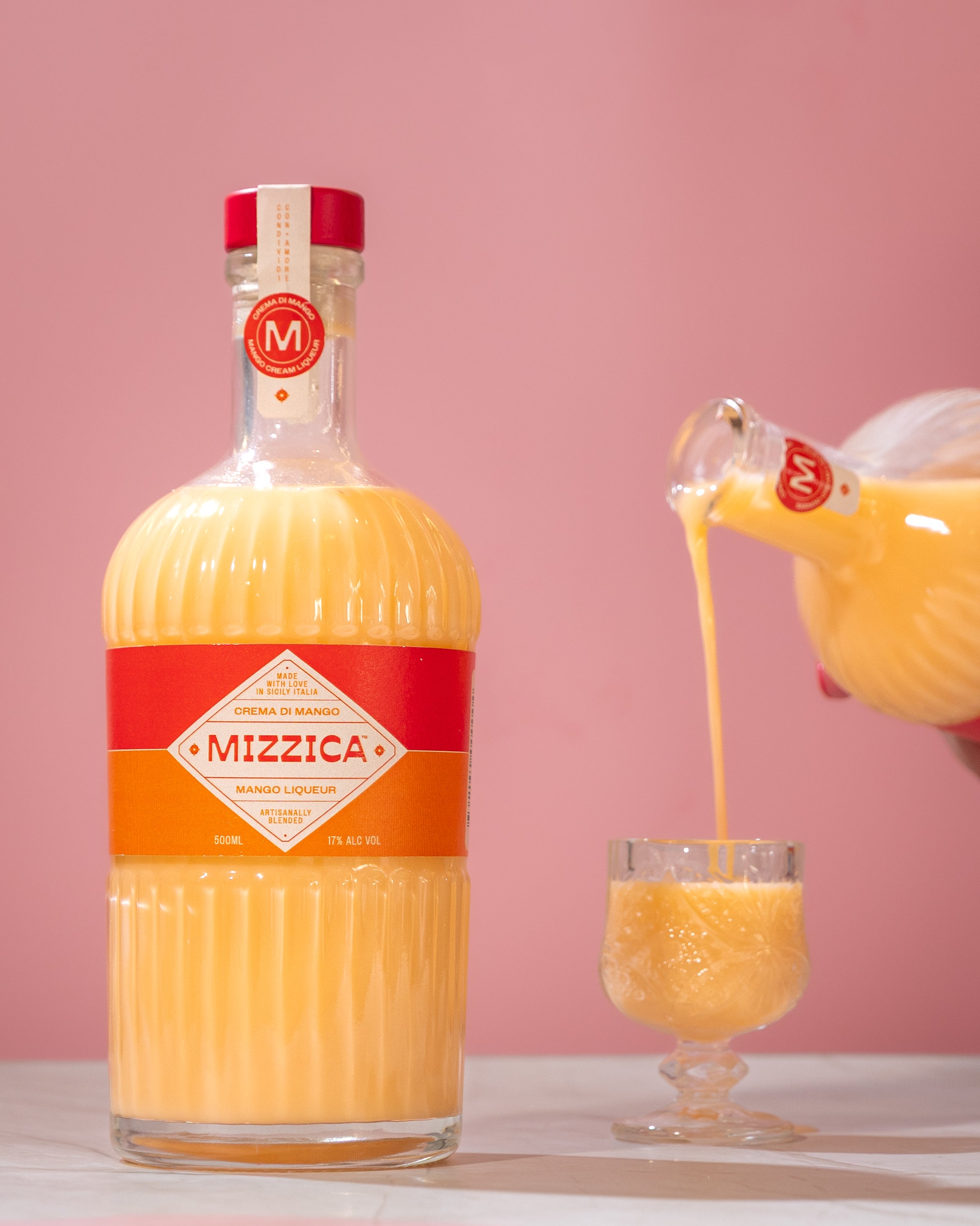 Mizzica mango liqueur bottle being poured into a glass with a pink background