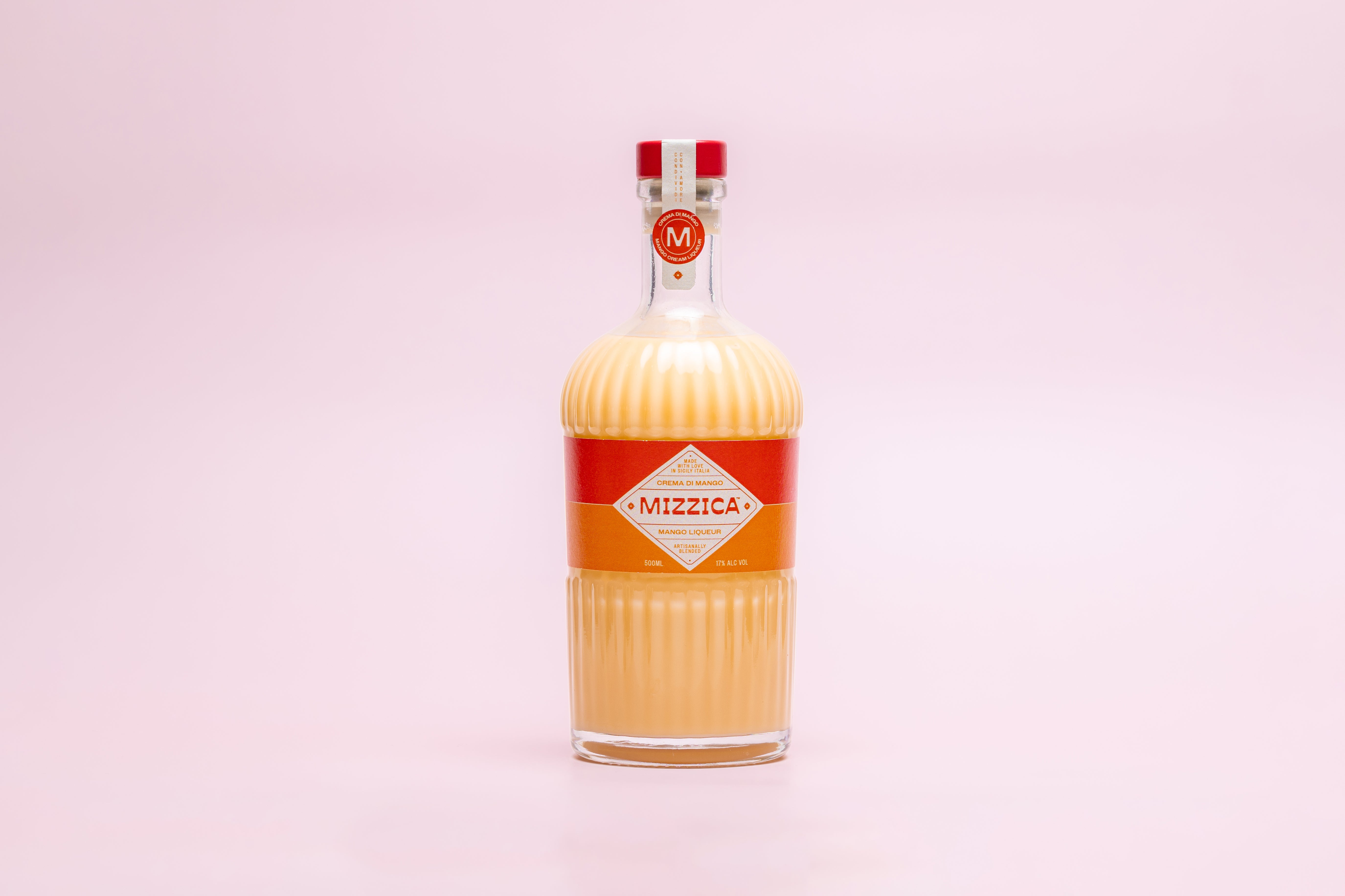 Bottle of Mizzica mango liqueur on a pink background