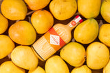Mizzica mango liqueur bottle surrounded by mangoes on a wooden surface