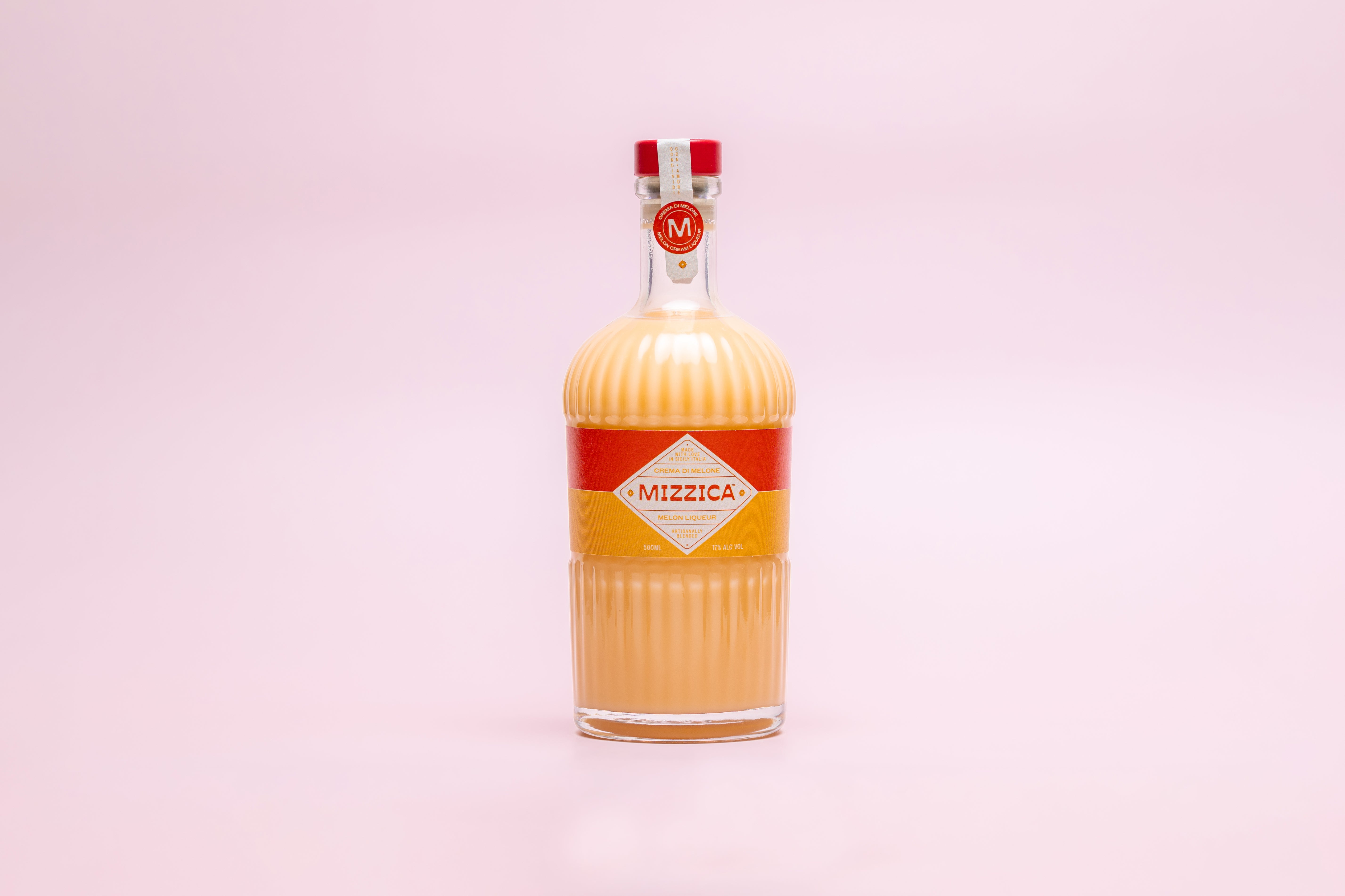 Bottle of Mizzica rockmelon liqueur on a pink background