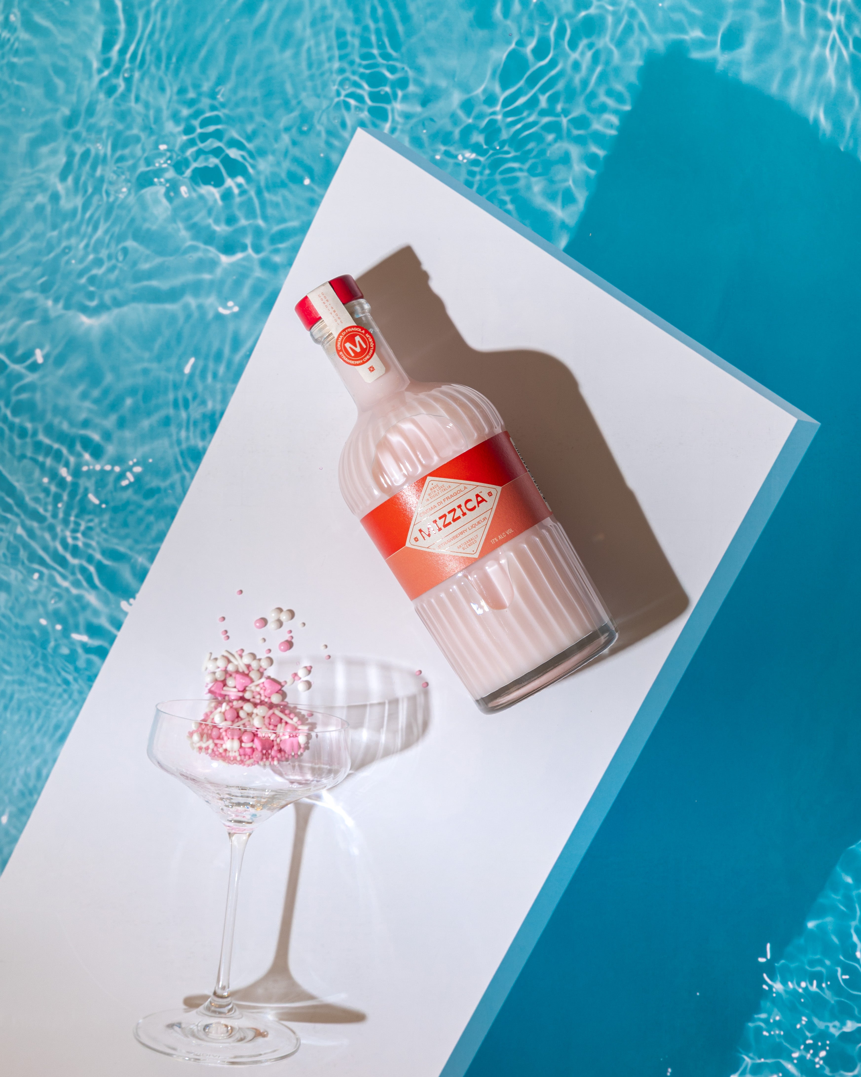 Mizzica strawberry liqueur bottle with a glass by a pool