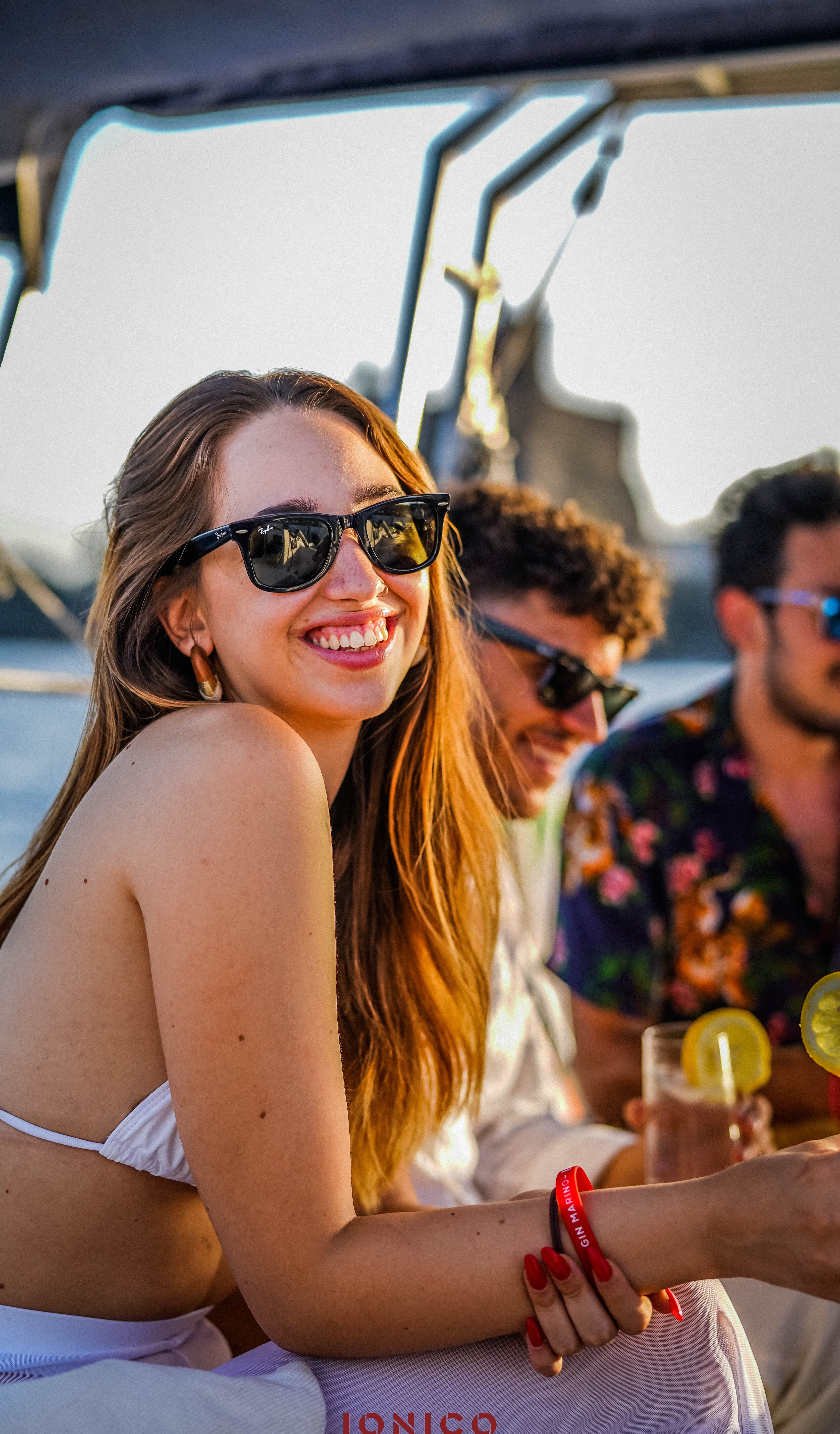 Woman wearing sunglasses and a white top, sitting outdoors with friends.