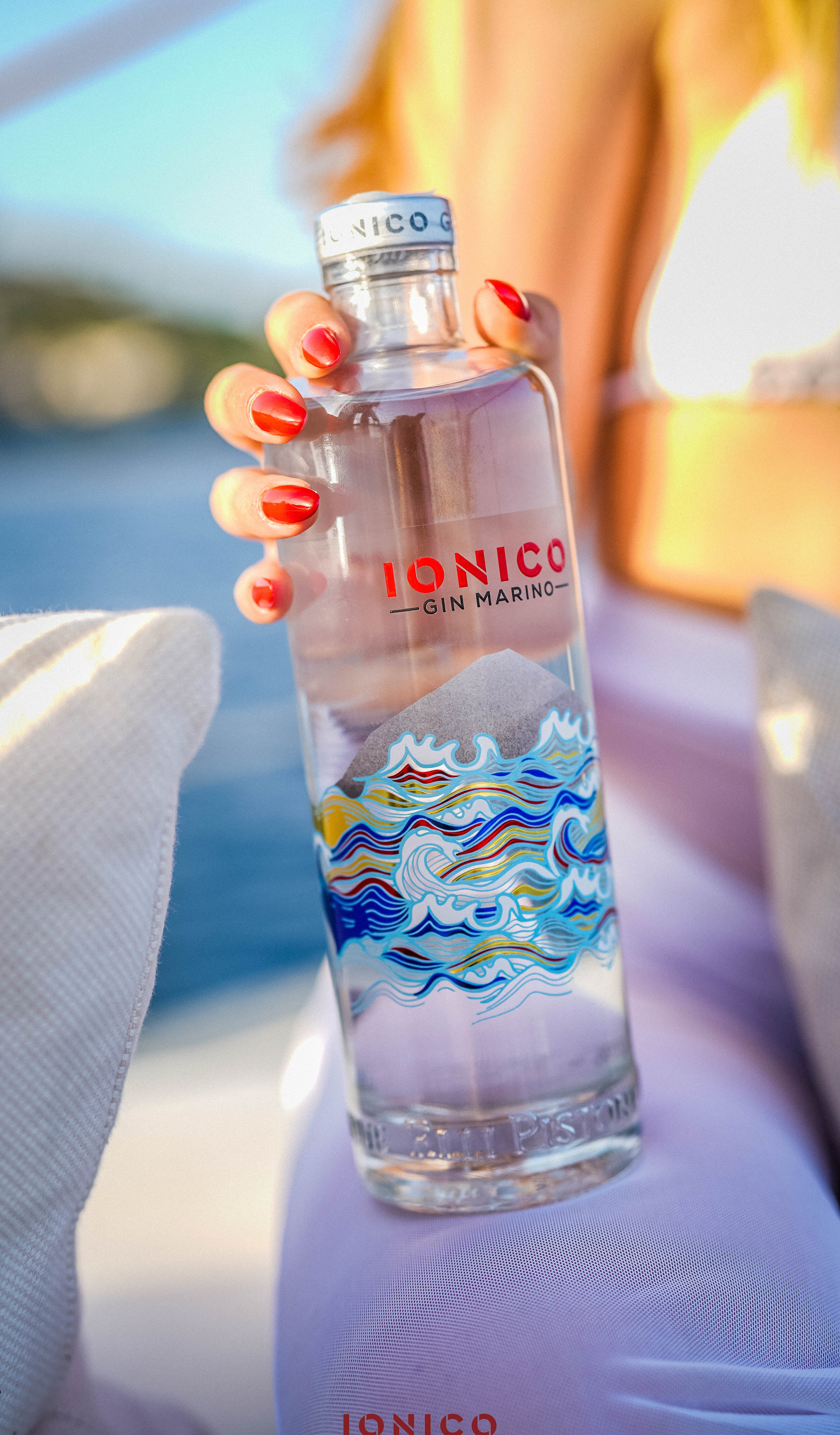 Person holding a bottle of Ionico gin with a scenic label.