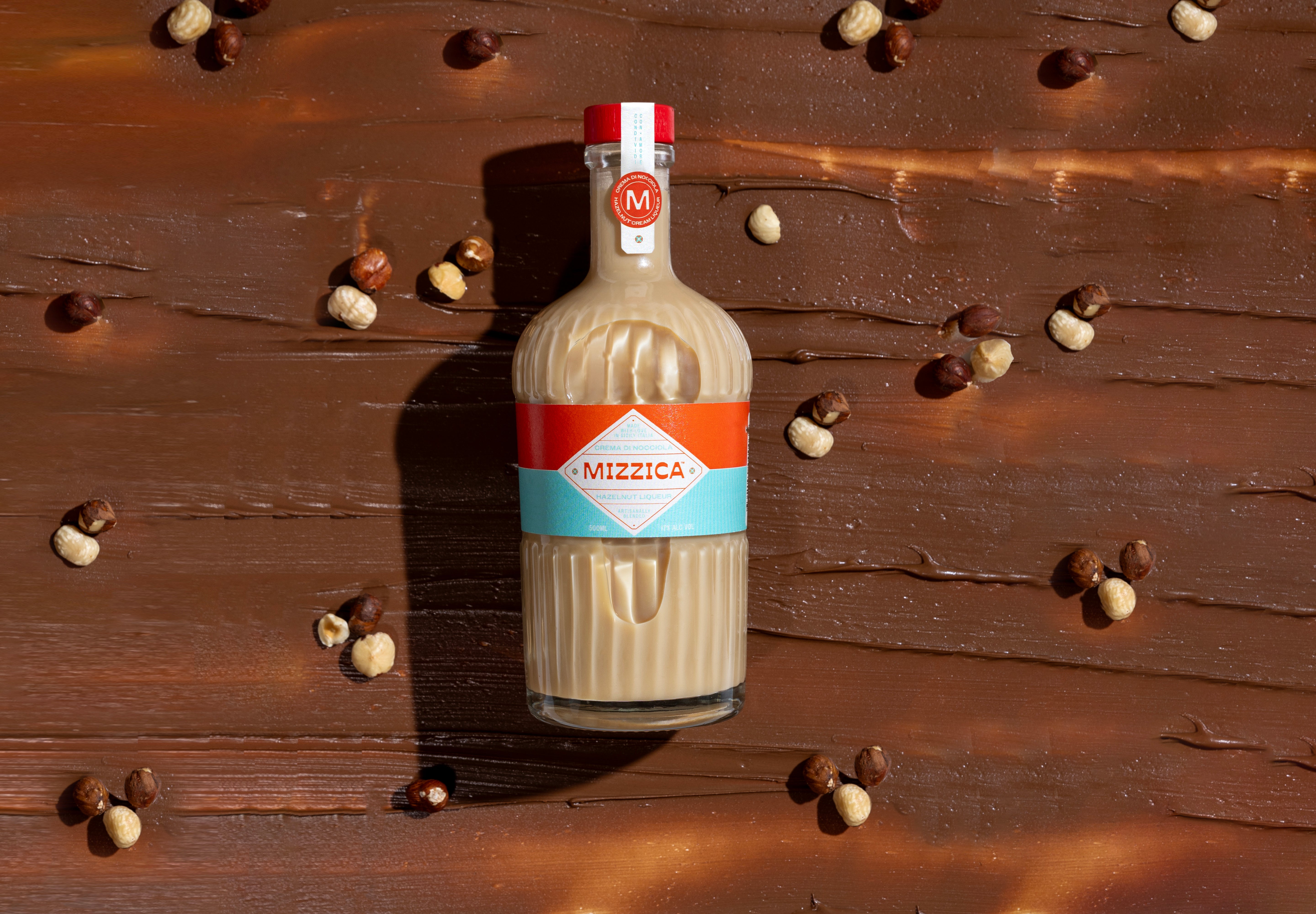 Bottle of Mizzica hazelnut liqueur on a chocolate surface with hazelnut pieces around