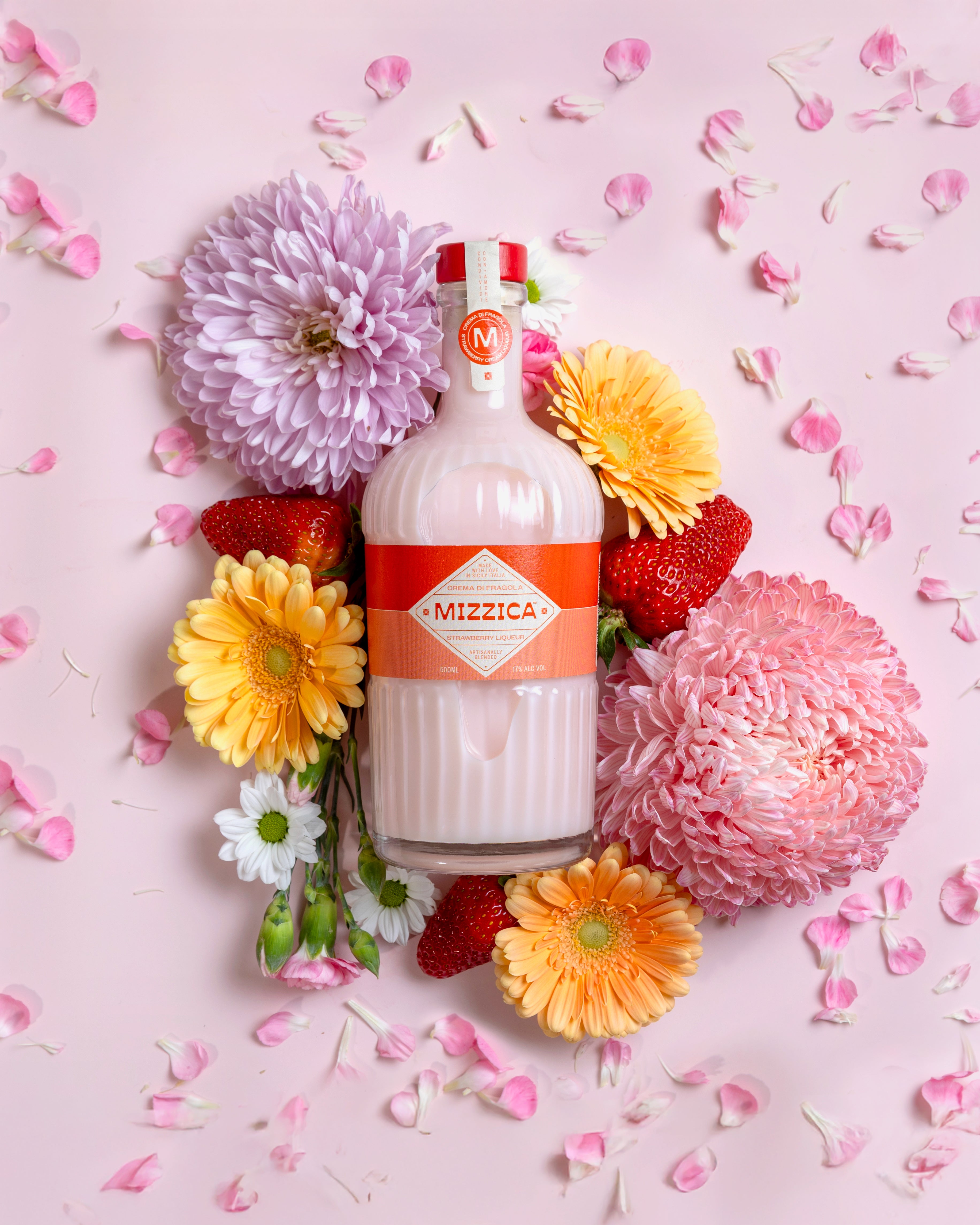 Mizzica strawberry liqueur bottle surrounded by flowers on a pink background